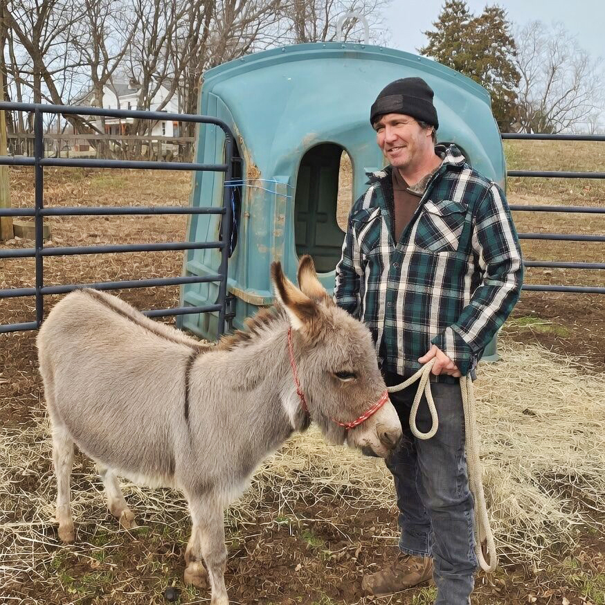 Billy, the trainer of Jet Crossing Stables & Sanctuary, posing with one of the donkeys in the pasture